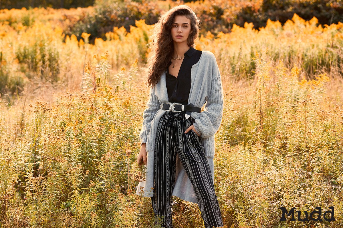 Model in grey cardigan and black patterned pants posing outdoors in a golden meadow by Soraya Dayani