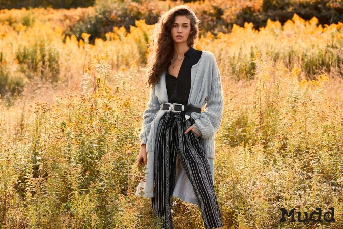 Model in grey cardigan and black patterned pants posing outdoors in a golden meadow by Soraya Dayani