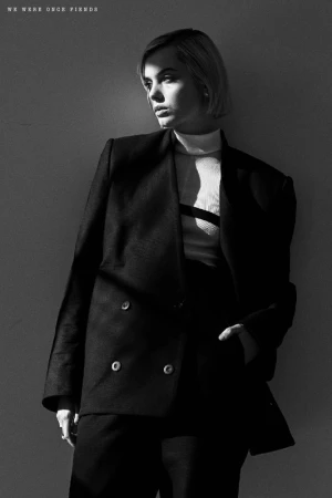 Monochrome portrait of a woman with short blonde hair wearing a dark oversized double-breasted blazer in stark directional lighting