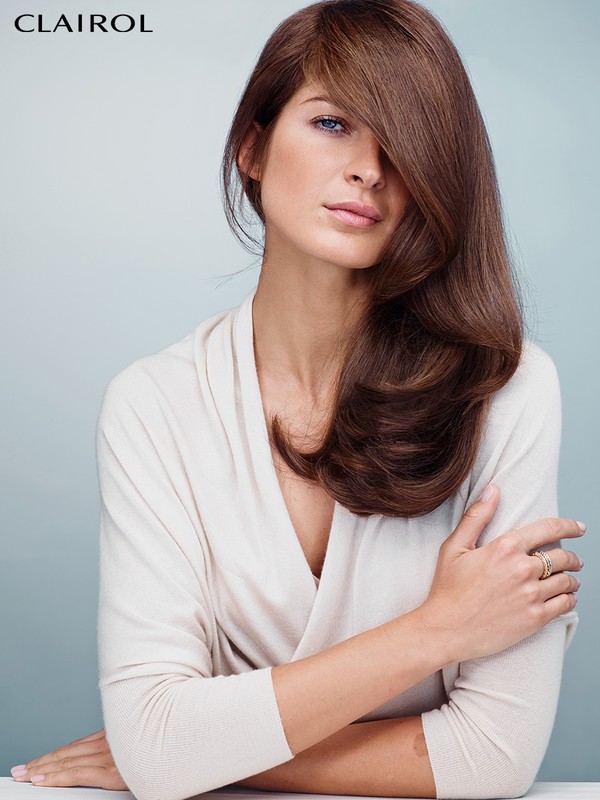 Woman with long brown hair partially covering her face wearing a cream top against a grey seamless background