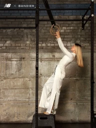 Blonde woman in white athletic wear holding gymnastic rings in a gym, styled by Soraya Dayani.