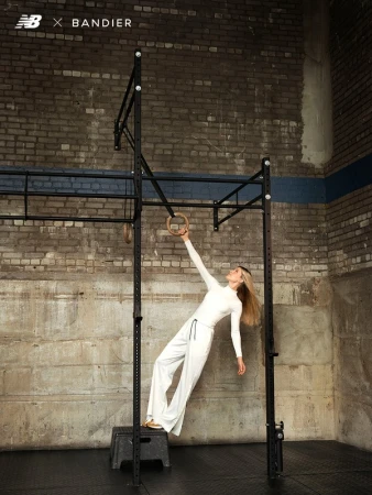 Woman in white long-sleeve top and white trousers holding gymnastics rings inside a gym, styled by Soraya Dayani.