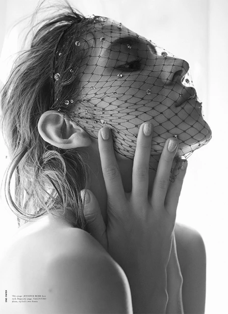 Monochrome close-up of a woman with fair skin and neutral nail polish, wearing a beaded fishnet veil and light makeup, gazing slightly down.