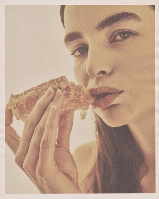 Close-up of a woman eating honeycomb, showcasing a natural beauty and connection to raw, organic food in a soft, golden-toned setting.