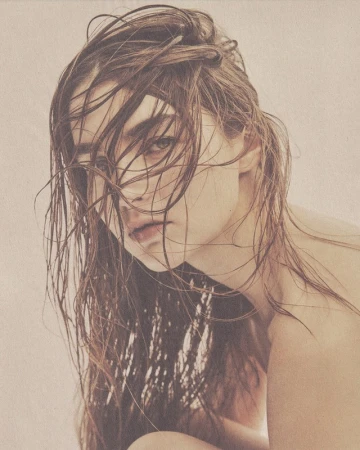 Close-up portrait of a woman with wet brown hair falling across her face in soft sepia tones.