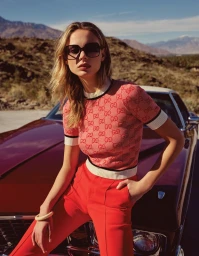 Model wearing oversized sunglasses and patterned top leaning on a vintage car in a desert mountain landscape.