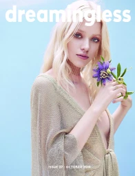 Blonde woman holding a purple flower wearing a metallic gold top against a solid blue background