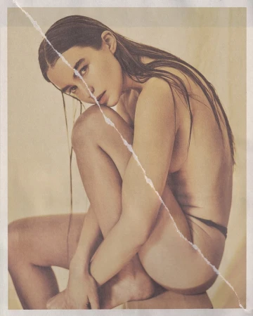 Portrait of a seated woman with long wet hair and a diagonal tear running across the printed photograph.