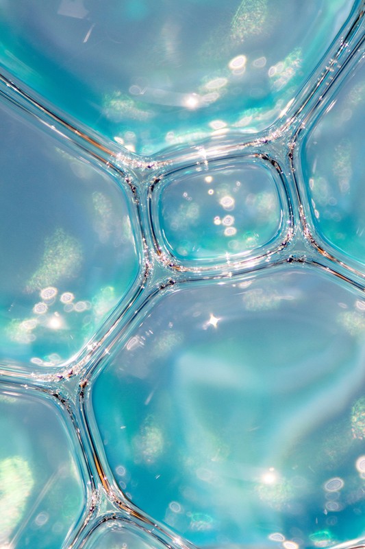 A macro abstract image of connected liquid cell structures in shades of blue, turquoise, and white, with a glossy, reflective surface.