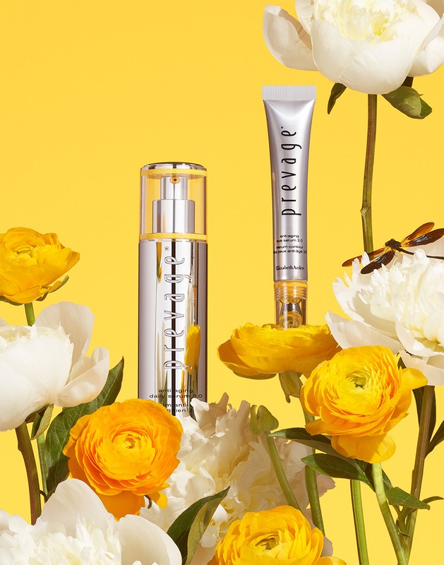 Cosmetic products from Prevage displayed with ranunculus and peonies in a bright yellow setting, ideal for beauty advertising.