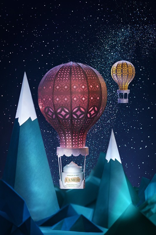 La Mer skincare cream in a hot air balloon basket, with a whimsical mountain and sky background; beauty and skincare concept.