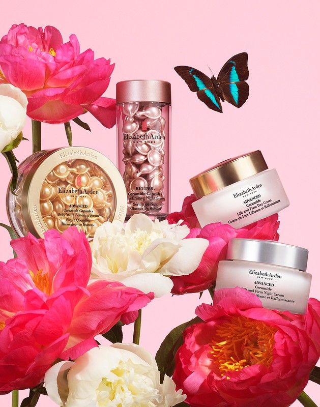 Elizabeth Arden skincare products, including retinol capsules and moisturizers, displayed with pink and white peonies and a butterfly on pink.
