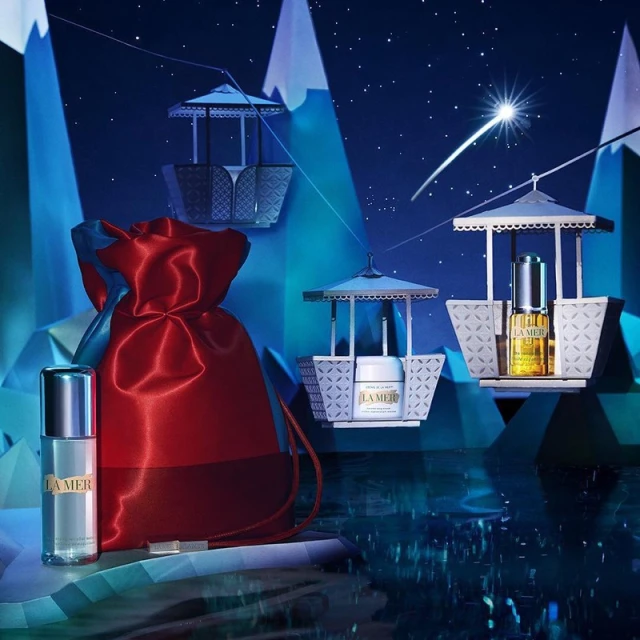 La Mer skincare products displayed in a wintry scene with a red drawstring bag and gondola-inspired product holders against a blue backdrop.