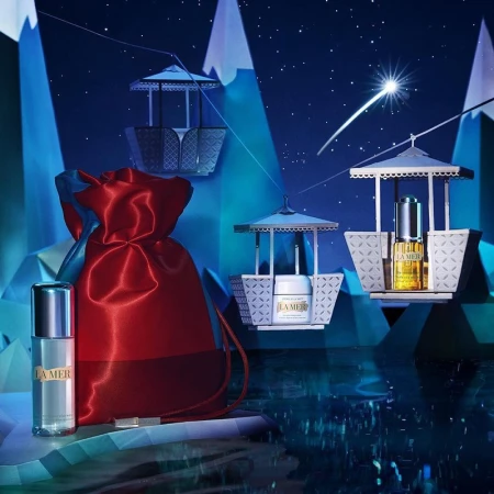 La Mer skincare products displayed in a wintry scene with a red drawstring bag and gondola-inspired product holders against a blue backdrop.