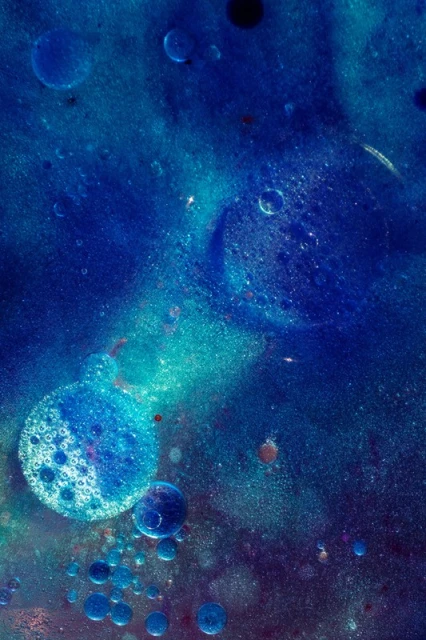 Abstract macro photograph of blue and teal colored bubbles, oil droplets, and liquid, creating a mesmerizing and artistic visual texture.