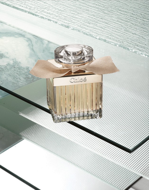 Chloe perfume bottle on reflective surface featuring its geometric glass design and tan ribbon detail.
