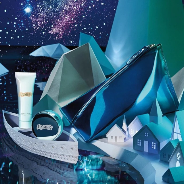 La Mer skincare products, including a tube, jar, and makeup bag, presented on a decorative boat with an abstract winter scene.