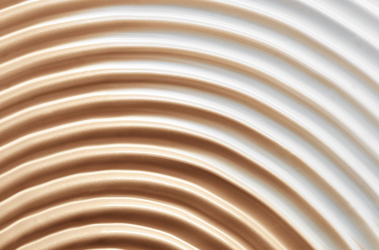 Close-up shot of light beige and white creamy textures forming semicircular waves. Great for beauty, cosmetic, or abstract backgrounds.