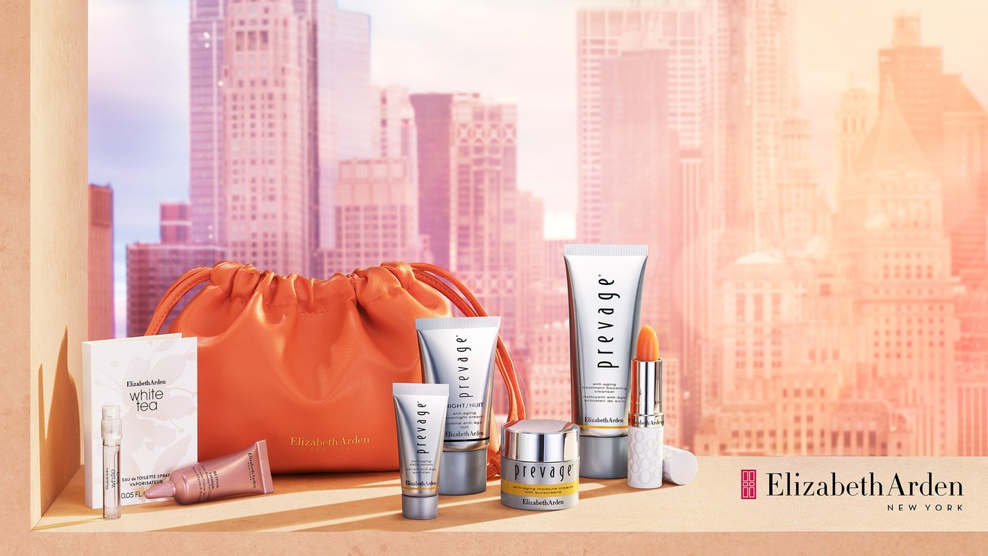 Elizabeth Arden skincare and cosmetic products arranged with an orange drawstring bag against a backdrop of blurred city buildings.