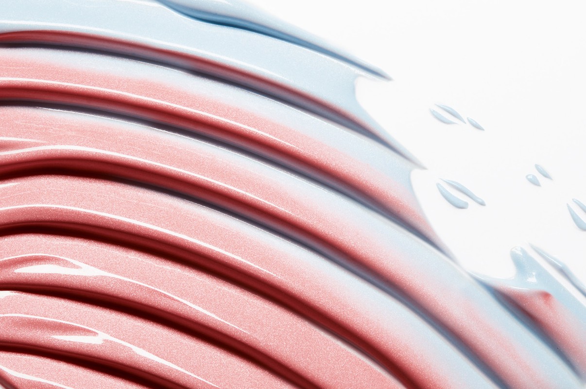 Abstract beauty product shot with light blue and red-toned smears in a parallel pattern on a white surface, providing a clean, modern feel.