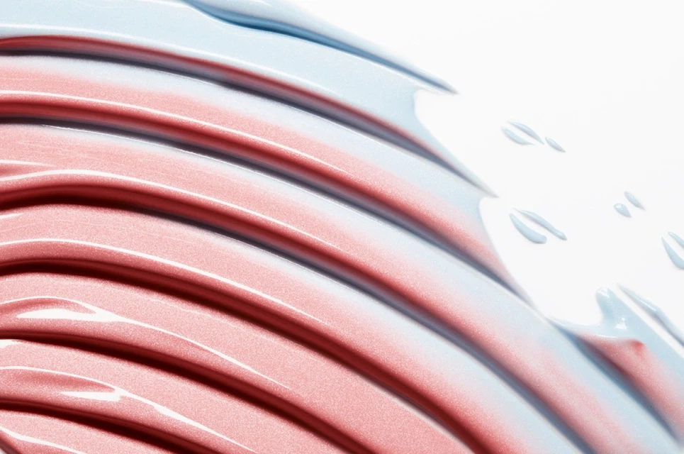 Abstract beauty product shot with light blue and red-toned smears in a parallel pattern on a white surface, providing a clean, modern feel.