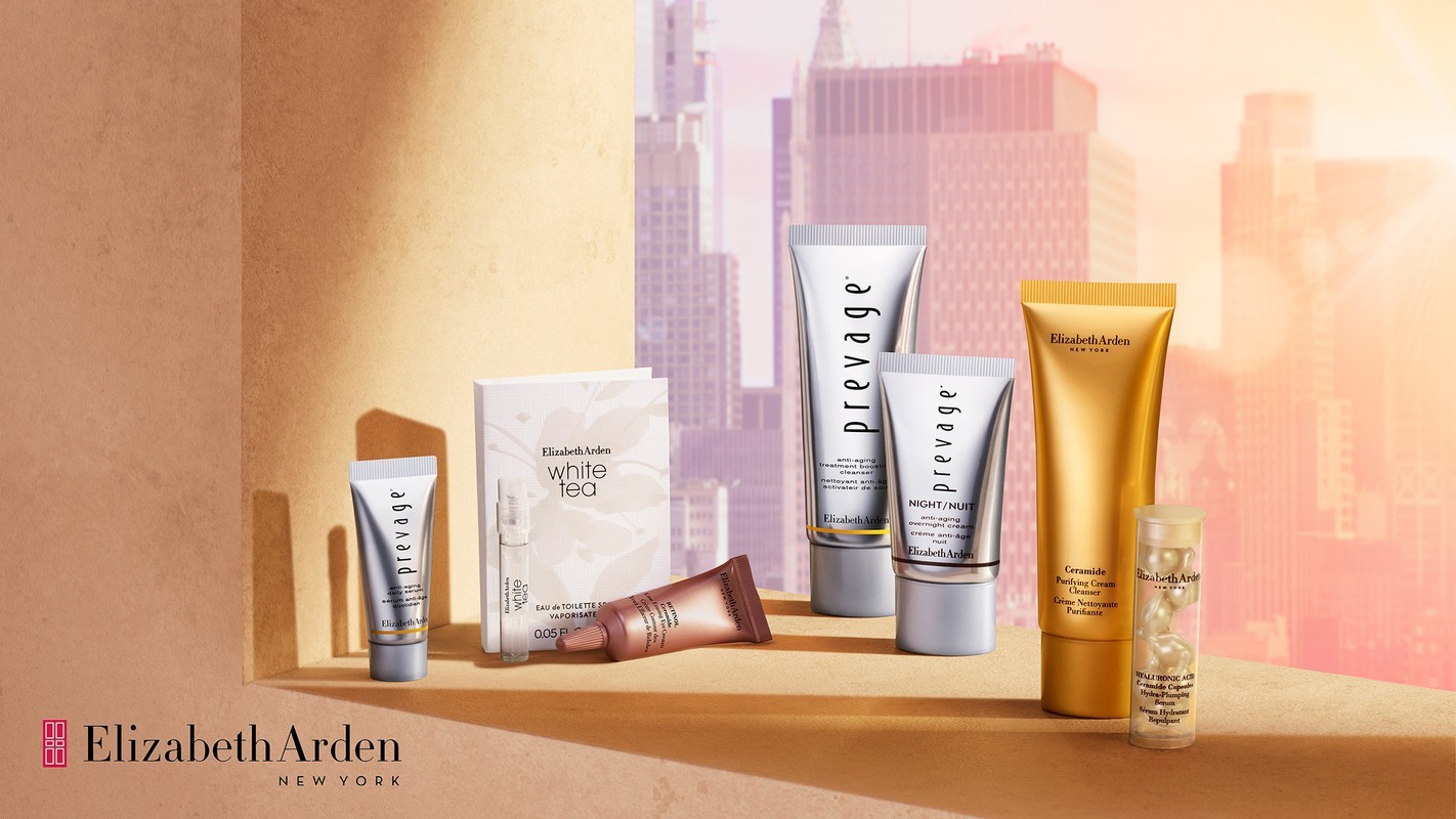 Collection of Elizabeth Arden Prevage and White Tea skincare products displayed on a shelf against a blurred cityscape backdrop.