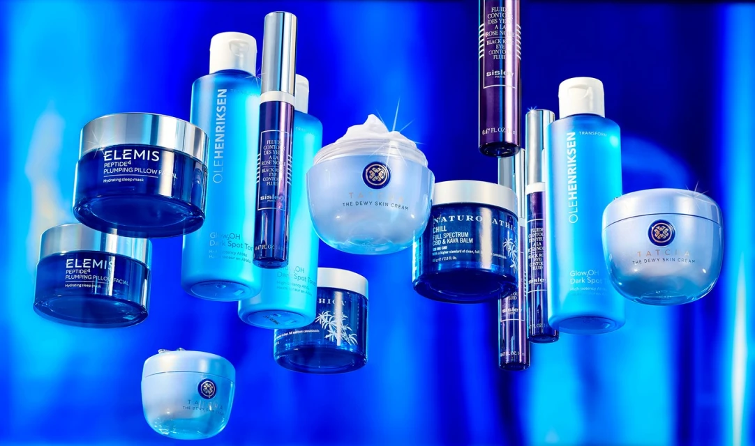 An array of blue-toned beauty products including creams, toners, and eye serums, arranged on a blue background. Brands are Elemis, Ole Henriksen, Tatcha.