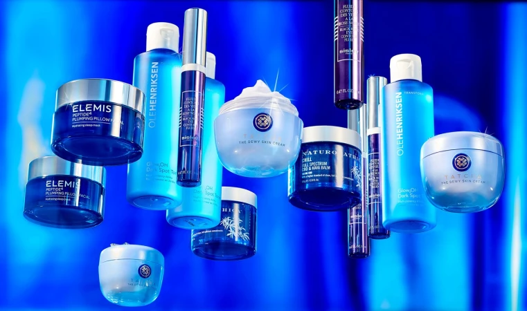 An array of blue-toned beauty products including creams, toners, and eye serums, arranged on a blue background. Brands are Elemis, Ole Henriksen, Tatcha.
