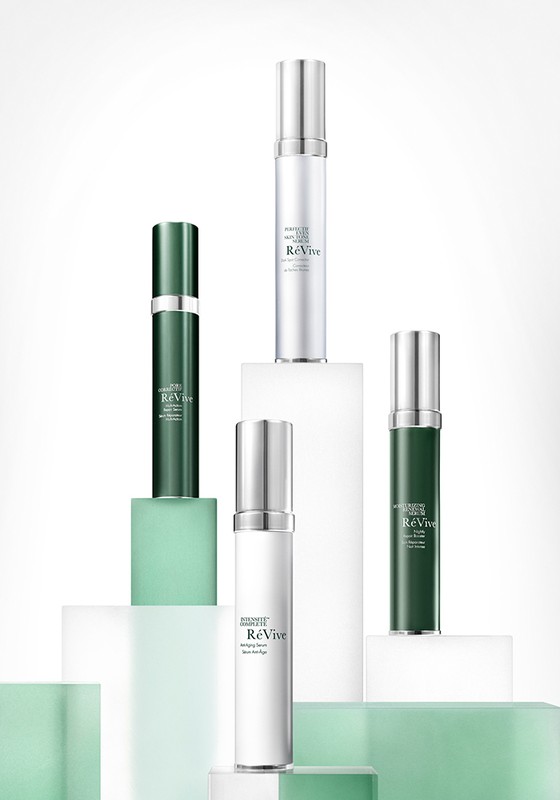 Five ReVive skincare bottles arranged on white and light green pedestals, showcasing a beauty product arrangement against a clean backdrop.
