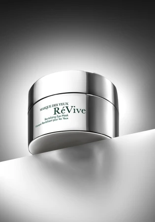 Silver container of ReVive revitalizing eye mask product on white surface with gray background in a product shot for beauty and skincare.