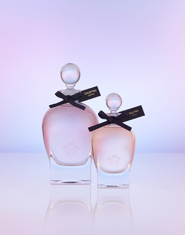 Two glass perfume bottles with spherical stoppers and black ribbon bows on a reflective surface against a gradient background.