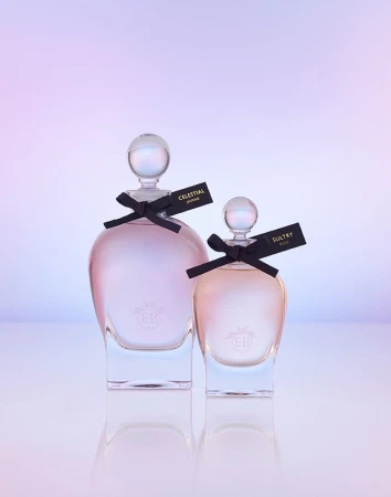 Two glass perfume bottles with spherical stoppers and black ribbon bows on a reflective surface against a gradient background.