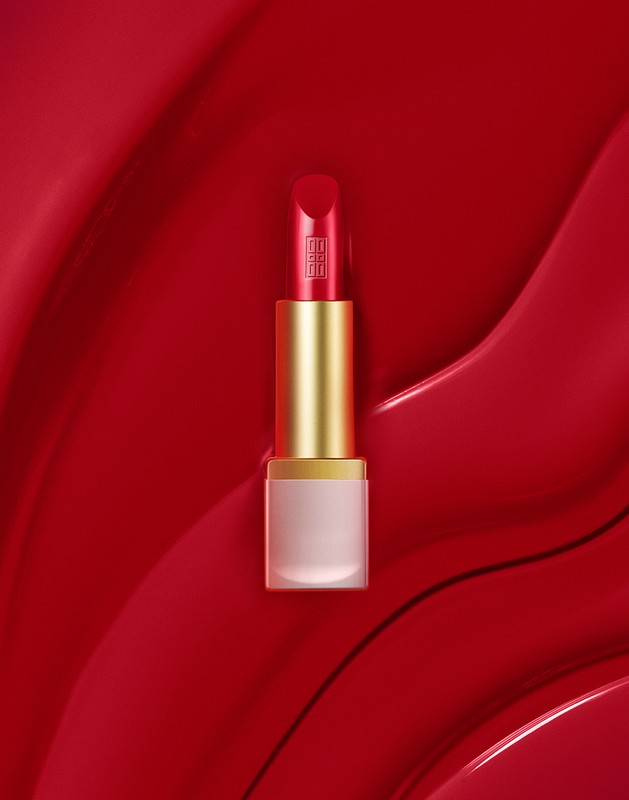 A red lipstick tube styled with prop styling by Alex Brannian set against a glossy red textured background.