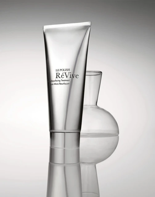 Silver tube of Le Polish ReVive skin resurfacing treatment alongside a transparent glass lab flask against a gradient background.
