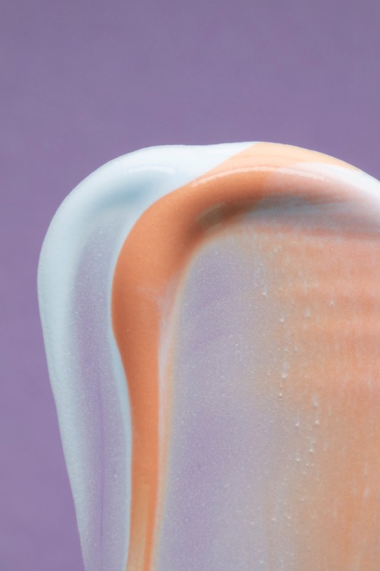 Macro shot of a colorful cosmetic cream swirl on a purple background, ideal for beauty and skincare product promotion, highlighting texture and color.