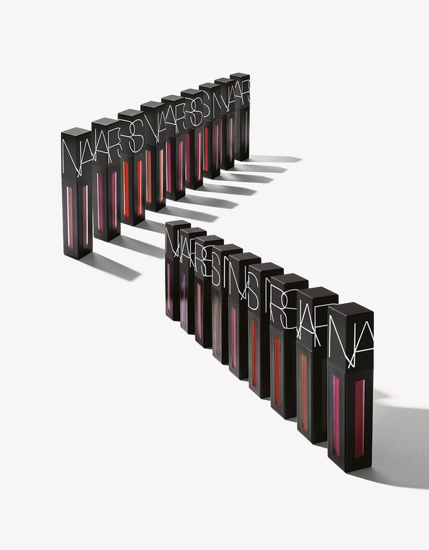 Row of NARS brand lip gloss products in black rectangular containers arranged against a white background with subtle shadows.