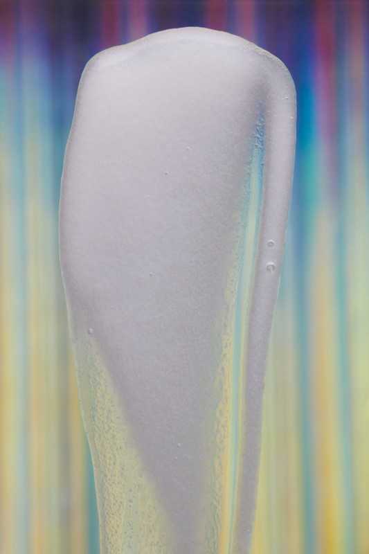 Close-up of translucent gel with light refraction and color gradients in a vertical format for beauty or cosmetic promotion.