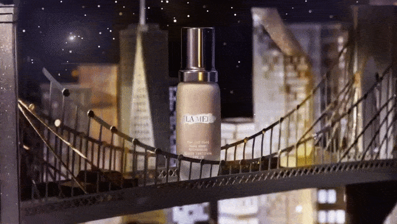 La Mer product shot with foundation bottle in front of a miniature bridge and city skyline backdrop with starry sky effect.