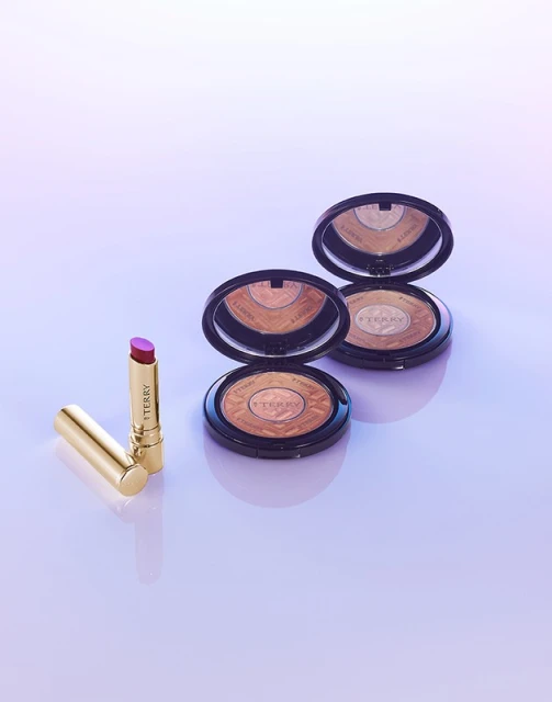 Cosmetics still life featuring lipstick and compact makeup on a glossy surface in cool lighting, showcasing beauty and elegance.