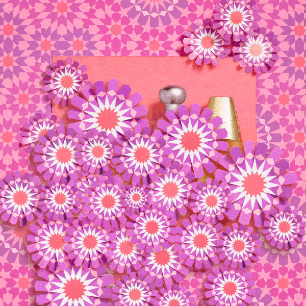 Still life of perfume bottles surrounded by patterned purple paper flowers against a geometric pink background, studio shot.