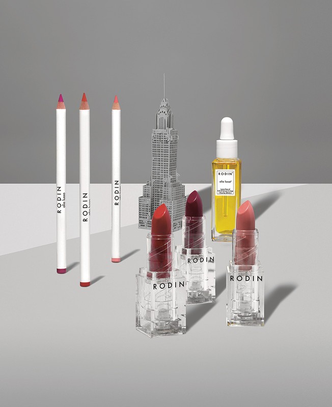 Rodin skincare and cosmetic product still life featuring lipsticks, lip pencils, face oil, and a miniature Empire State Building.