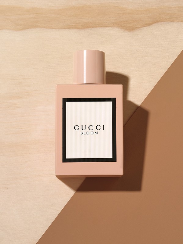 Close-up of a pink Gucci Bloom perfume bottle on a background of wood and brown tones in a studio setting.