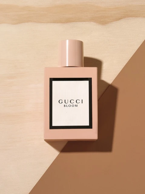 Close-up of a pink Gucci Bloom perfume bottle on a background of wood and brown tones in a studio setting.