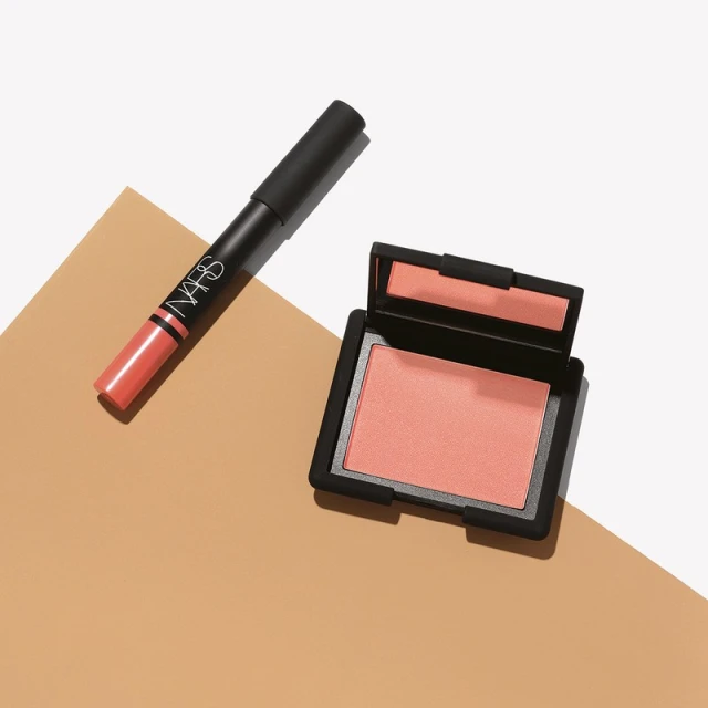 NARS makeup product set featuring blush compact and lipstick stick on a neutral tan and white background in a studio setting.