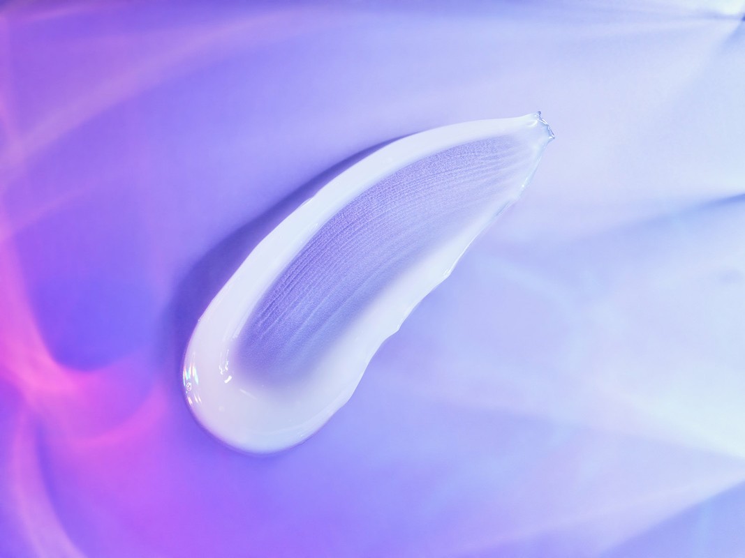 Close-up of white cream swatch on a smooth purple and blue background with soft lighting, highlighting texture and product quality.