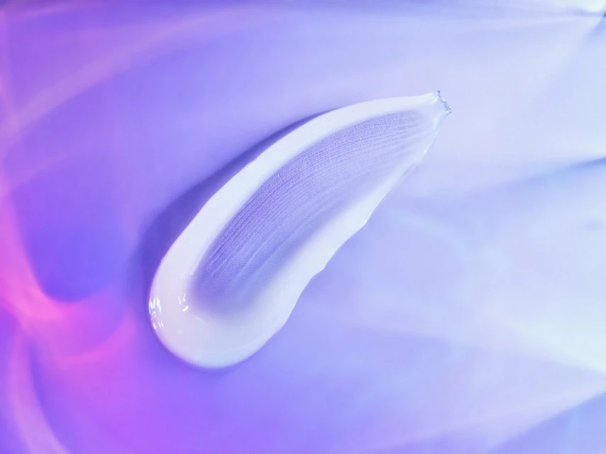 Close-up of white cream swatch on a smooth purple and blue background with soft lighting, highlighting texture and product quality.