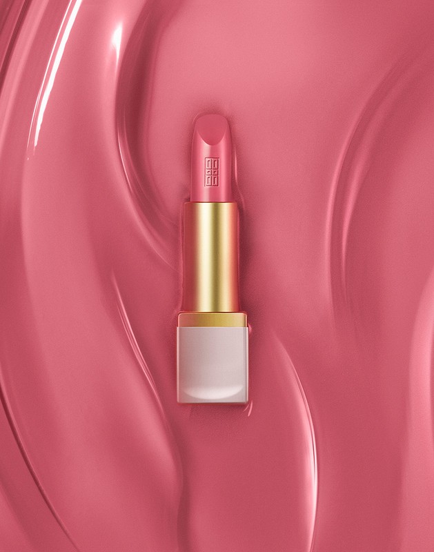 Close-up of a pink lipstick tube with a gold band set against a wavy background of matching pink makeup, product shot.