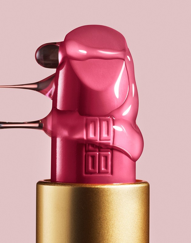 Close-up of pink lipstick tube with dripping pink liquid on light pink background, showcasing beauty and cosmetic product photography.