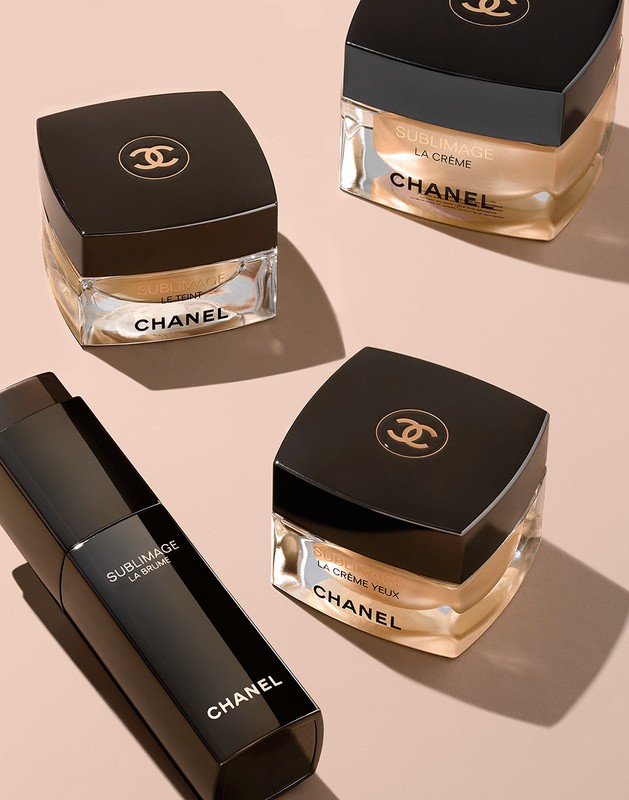 Several jars and a bottle of Chanel Sublimage skincare products are arranged on a light peach-colored surface in a studio setting, product photography.
