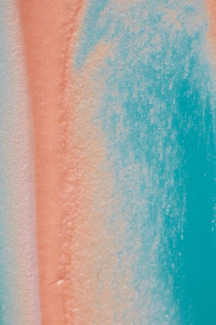 Abstract close-up of light turquoise and coral colors blending, creating a textured, marbled appearance with subtle tonal gradations.